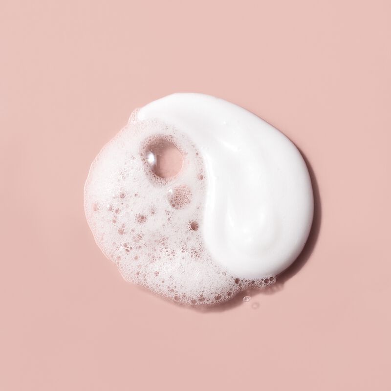 White lotion and foamy lather layered together on a soft pink background