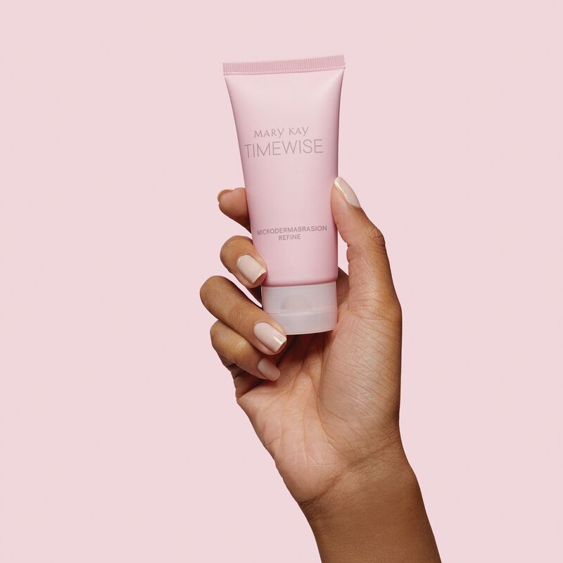 Mediumskinned hand holding TimeWise Microdermabrasion Refine against pink background