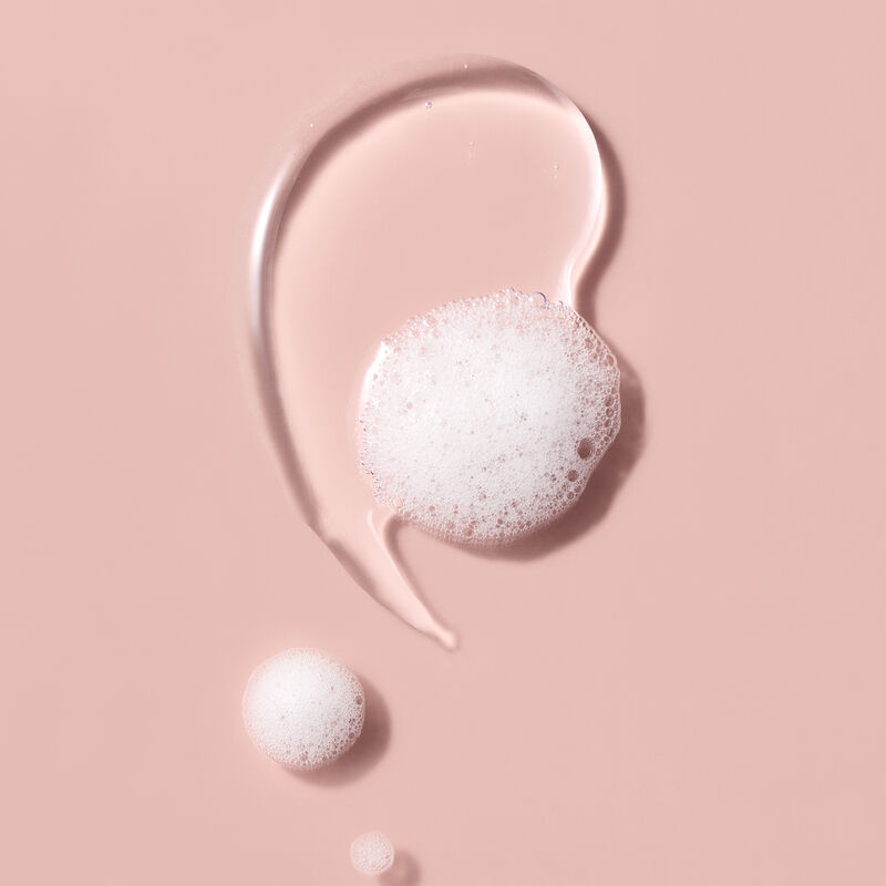 Foamy bubbles and body wash texture swirled across a soft pink background