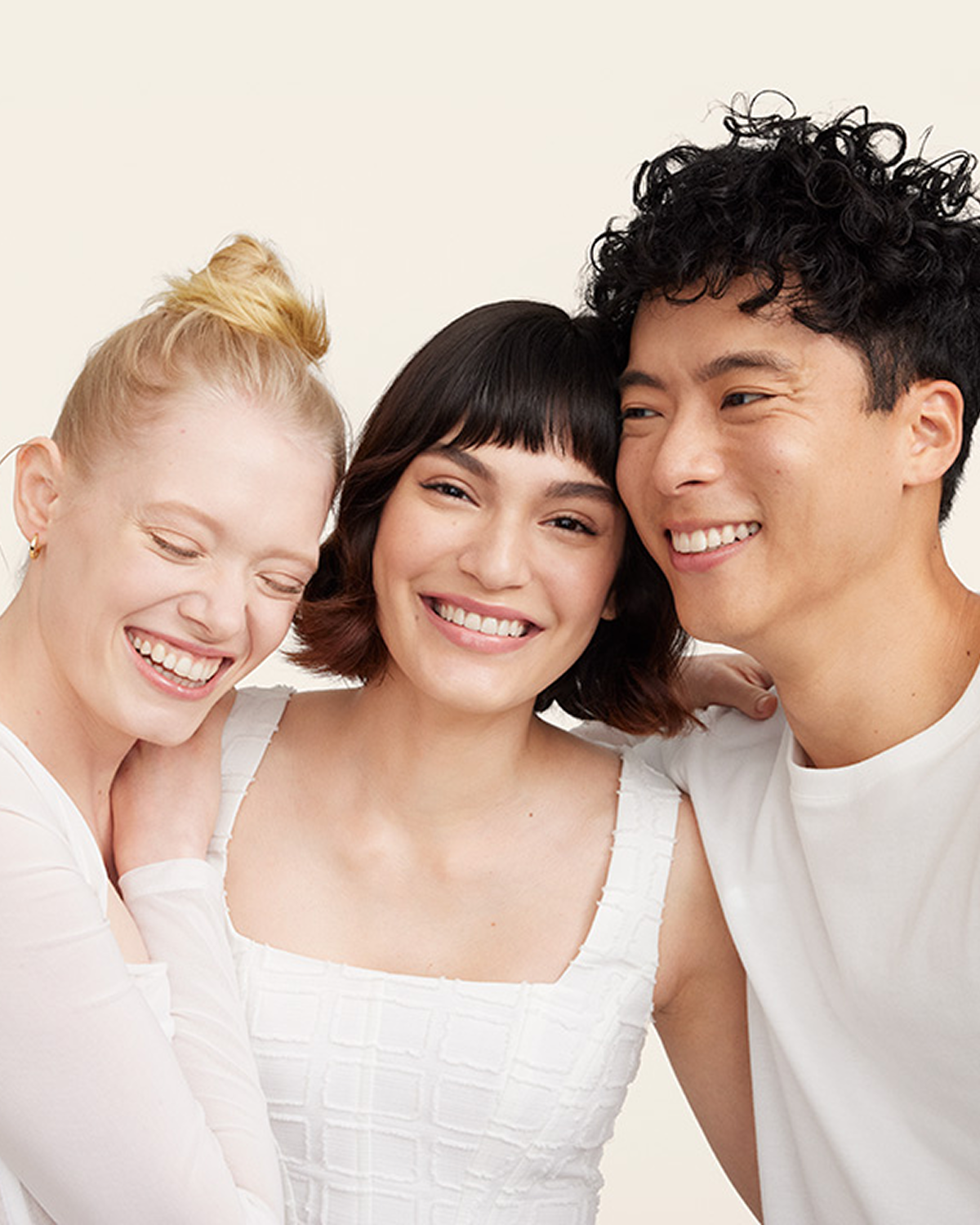 A group of people smiling, dressed in shades of white against a beige background.