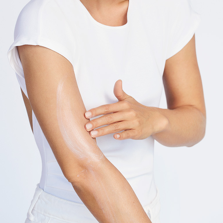 Model with medium skintone applying Mary Kay SPF 50 sunscreen to upper arm