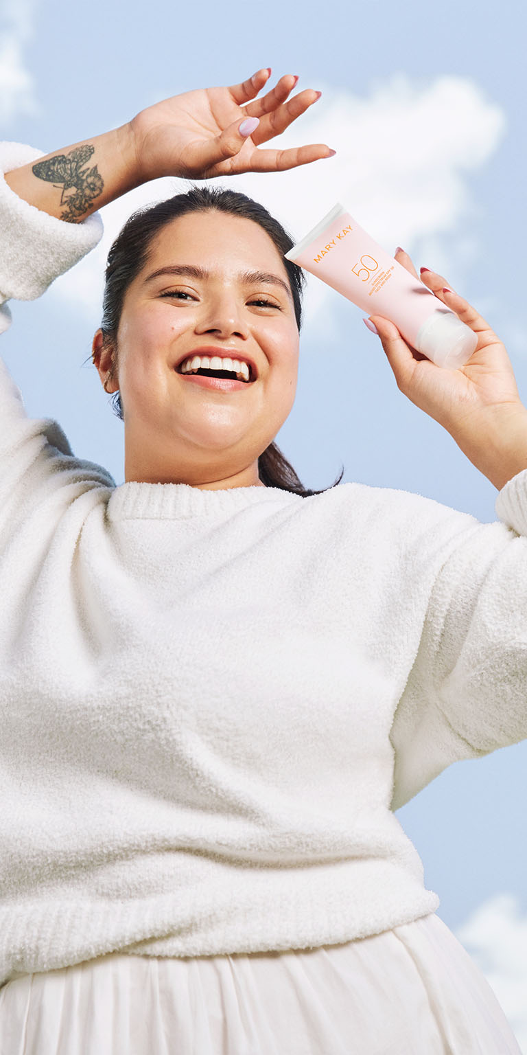 Model holding Mary Kay Sunscreen Broad Spectrum SPF 50 under blue sky